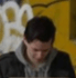 A person with dark hair looks down against a graffiti-covered wall.